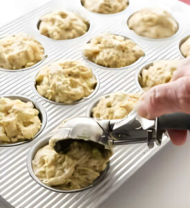 Scooping muffin batter into a baking pan.