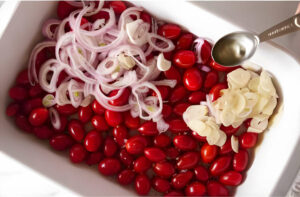 Adding cherry tomatoes to a baking dish with shallots and garlic.
