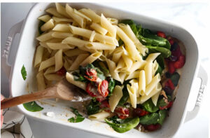 Stirring pasta and spinach into the roasted tomatoes and goat cheese.