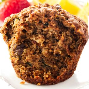 A partially eaten morning glory carrot apple muffin on a plate.