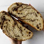 Two hands holding a loaf of dutch oven cinnamon raisin bread.