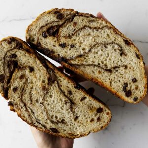 Two hands holding a loaf of dutch oven cinnamon raisin bread.