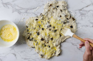 Brushing egg wash over raisin bread dough.