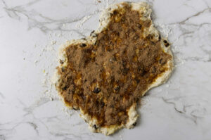 Scattering cinnamon sugar over a stretched out slab of raisin bread dough.