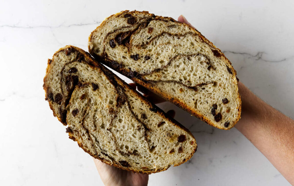 Hands holding two halves of a cinnamon raisin bread that was baked in a Dutch oven.