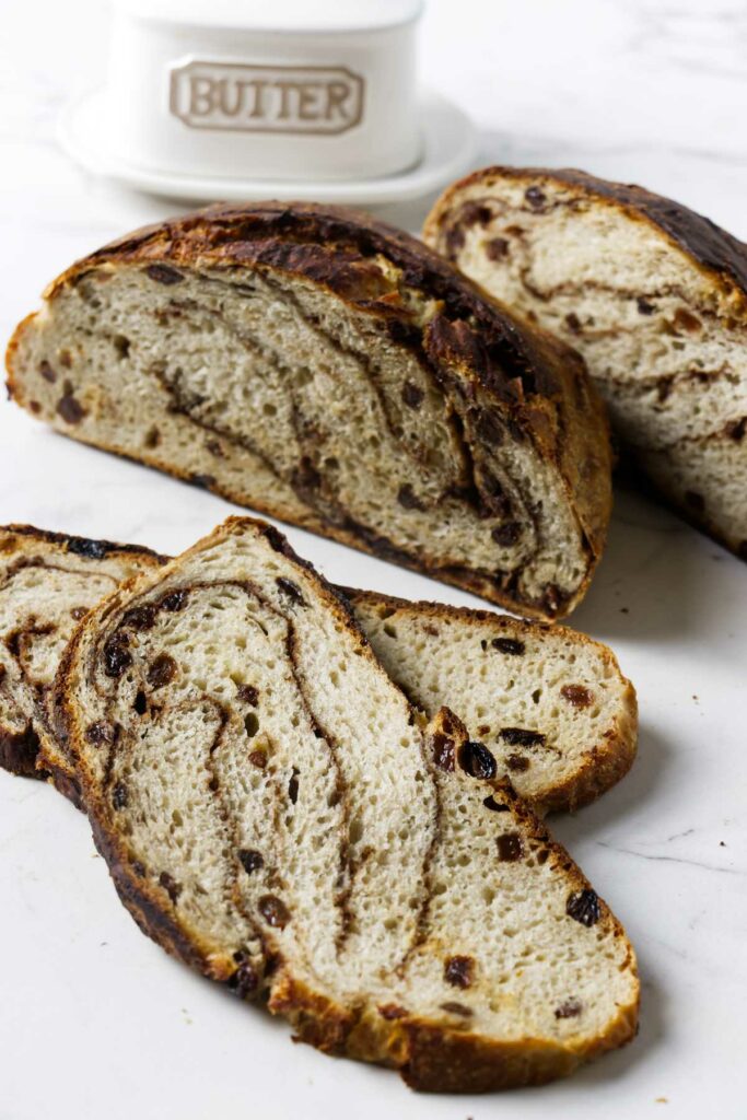 A boule loaf of no knead cinnamon swirl raisin bread in front of a tray of butter.