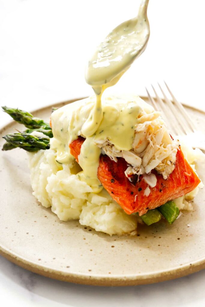 Drizzling bearnaise sauce over salmon oscar on a plate.