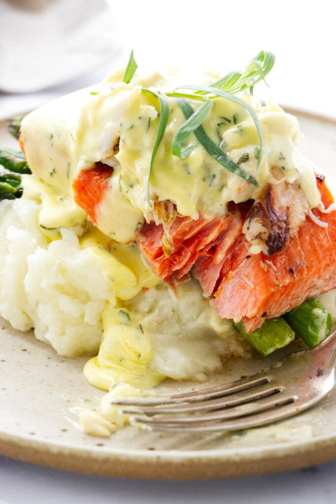 A fork in front of a serving of salmon oscar with mashed potatoes.
