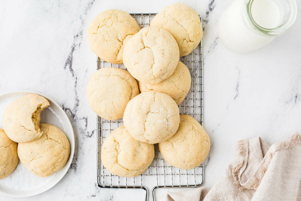 A pile of sourdough discard sugar cookies on a rack next to a jar of milk.