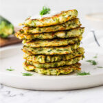 A stack of eight sourdough discard zucchini fritters on a plate.