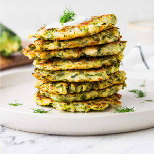 A stack of eight sourdough discard zucchini fritters on a plate.