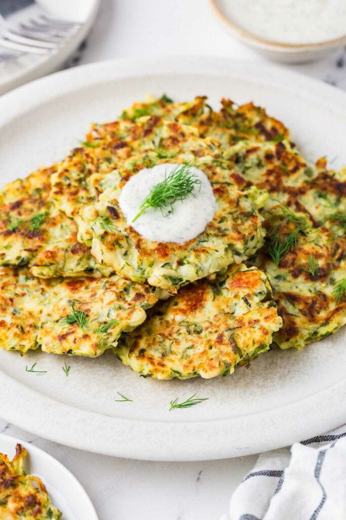 Several zucchini fritters topped with sour cream.