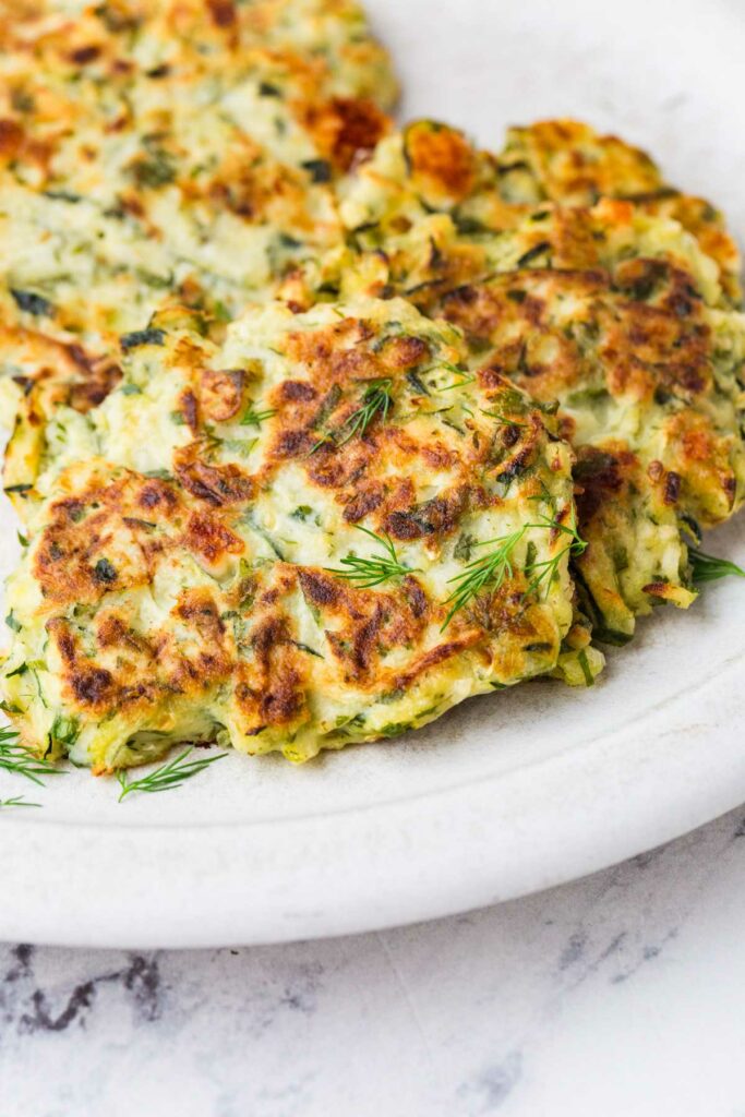 Sourdough zucchini fritters on a plate with fresh dill.
