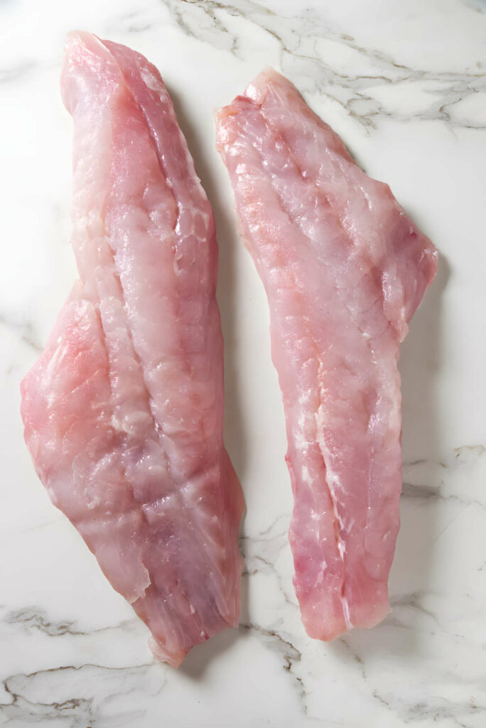 Two large uncooked rockfish fillets on a white counter.