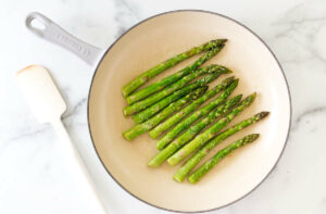 Asparagus spears in a skillet next to a white spatula.
