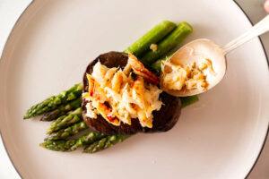Spooning crab meat on top of a steak.