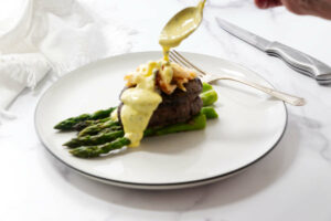Drizzling hollandaise sauce over steak and crab.
