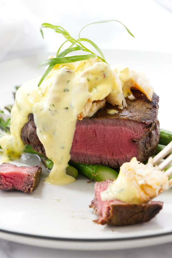 A slice of steak in front of layered steak oscar on asparagus.