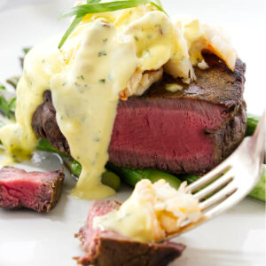 A fork holding a bite of steak with bearnaise sauce and crabmeat.