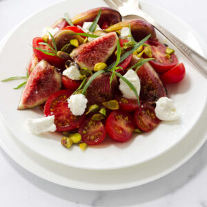 A fig and tomato salad on a plate with a fork.