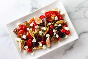 Cheese and pistachios on top of a tomato fig salad.