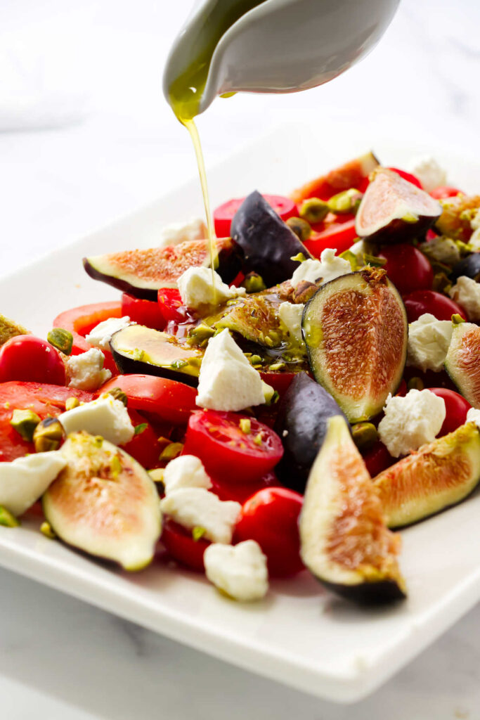 Pouring vinaigrette over a fig and tomato salad.