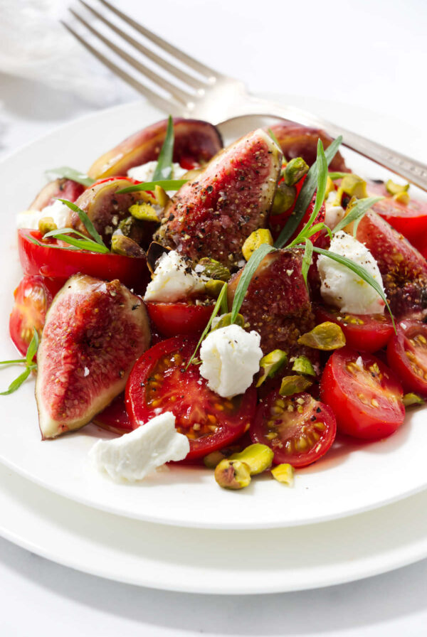 A fig and tomato salad on a plate with tarragon leaves.