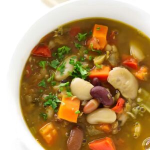 Bowl of vegetable soup with beans, carrots, herbs, and parsley garnish.
