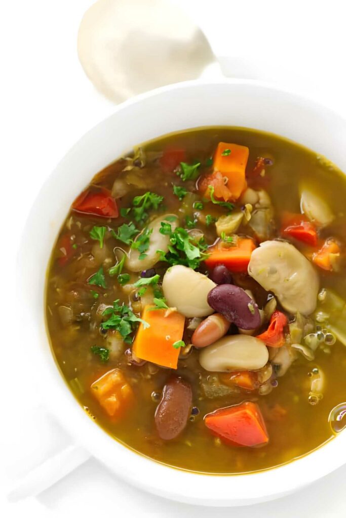 Bowl of vegetable soup with beans, carrots, herbs, and parsley garnish.