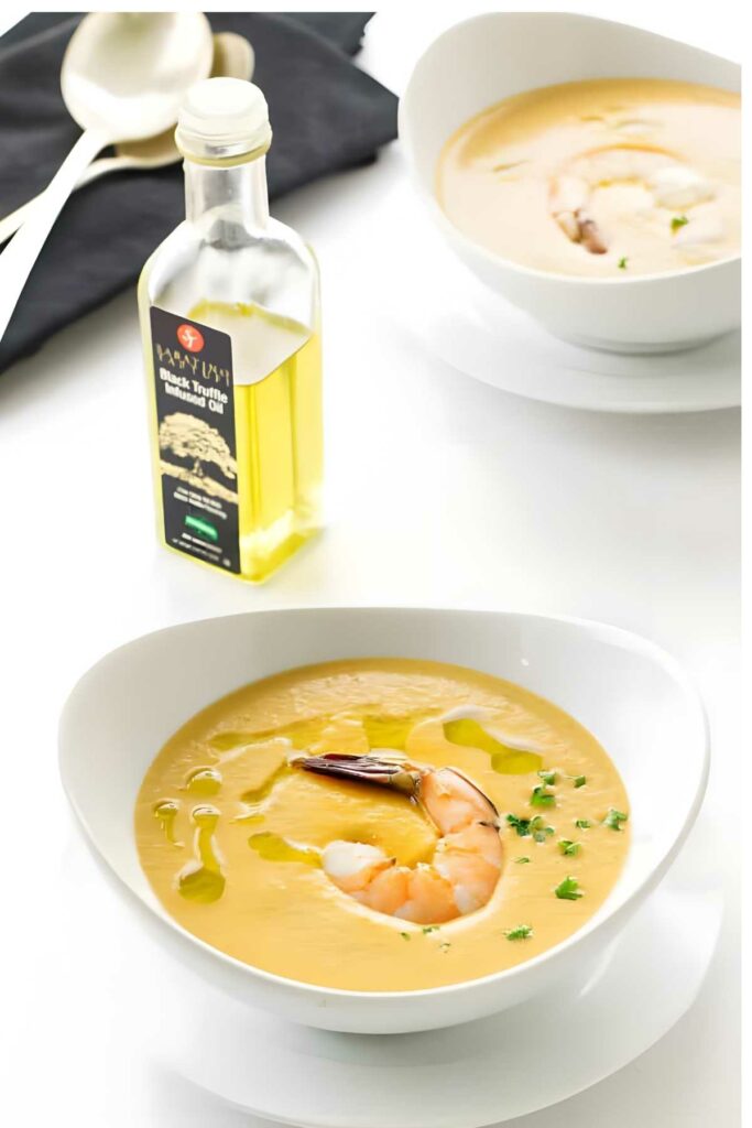 White bowl of shrimp soup with shrimp and herbs on a white surface.