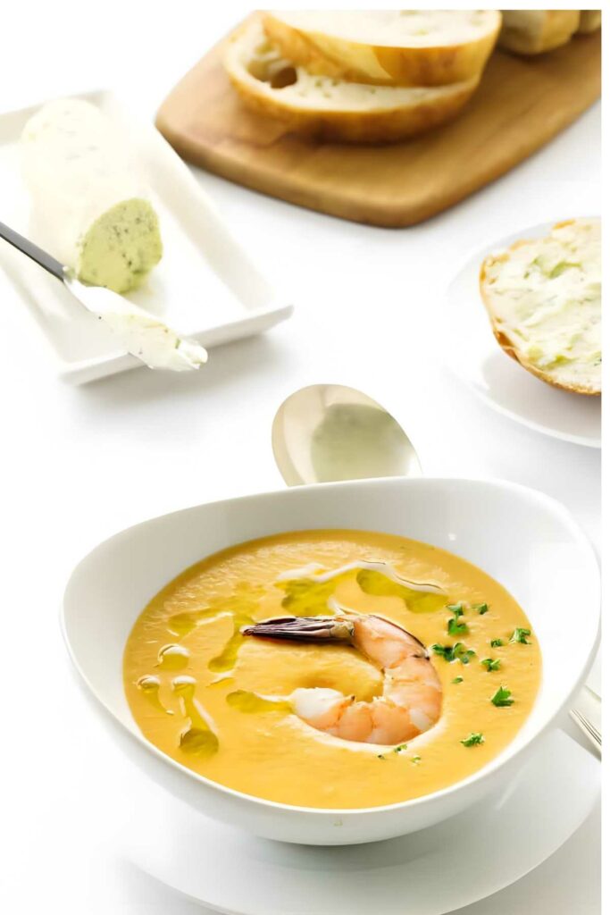 Creamy shrimp bisque soup with shrimp and herbs, bread and butter in background.