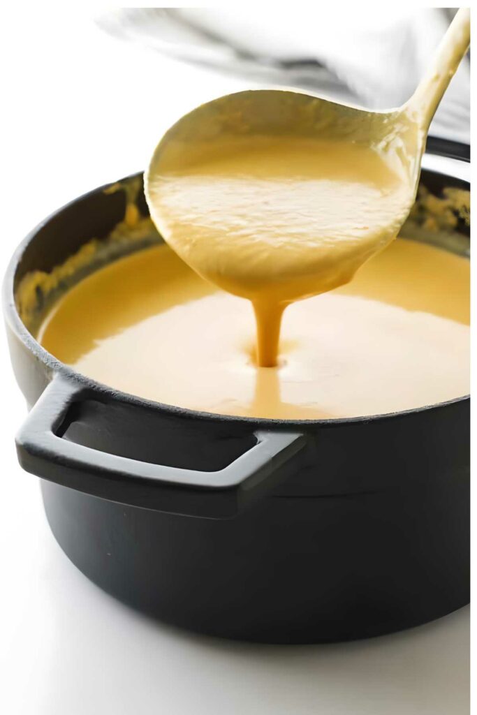 Ladle lifting thick shrimp bisque from a black pot.