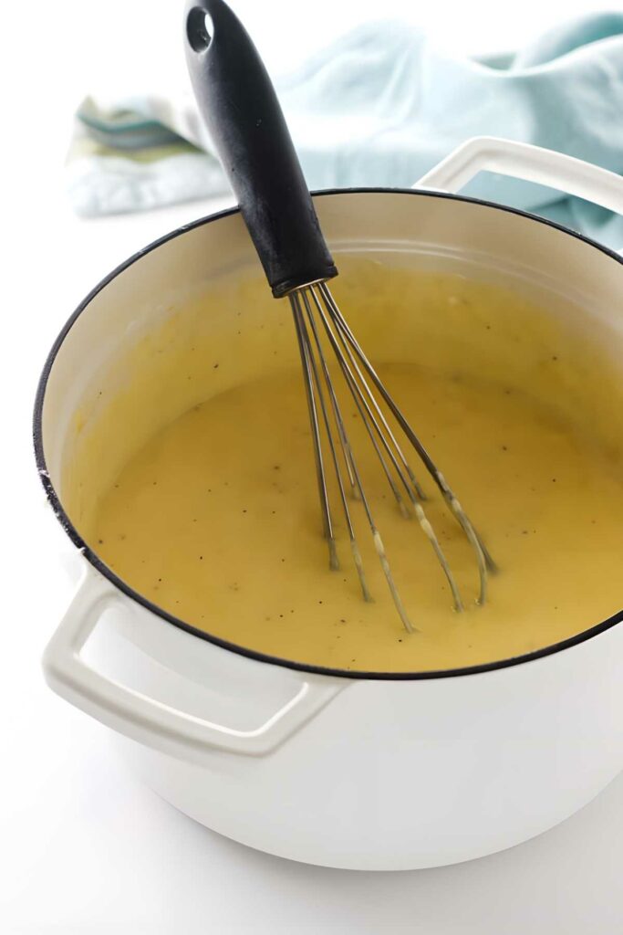 White pot of creamy cheese sauce with a whisk inside.