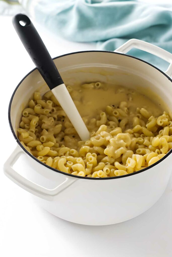 White pot of creamy macaroni and cheese with a spatula inside.