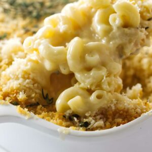 Creamy macaroni and cheese with crispy breadcrumbs being scooped from a baking dish.