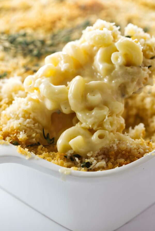Creamy macaroni and cheese with crispy breadcrumbs being scooped from a baking dish.