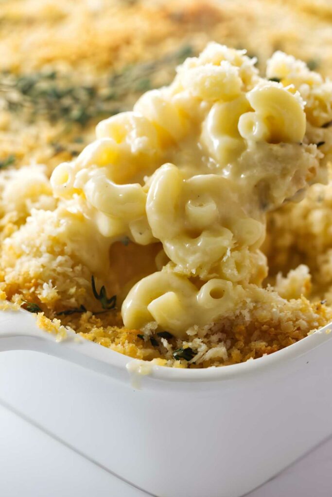 Creamy macaroni and cheese with crispy breadcrumbs being scooped from a baking dish.