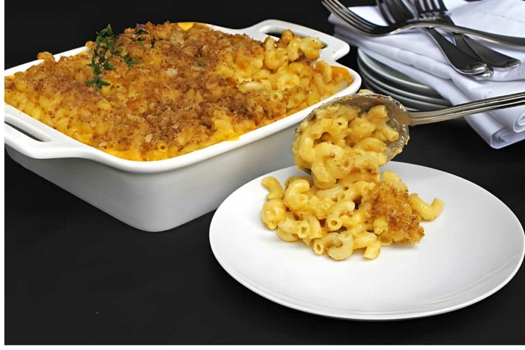 Spoon scooping mac and cheese with breadcrumbs onto a white plate.