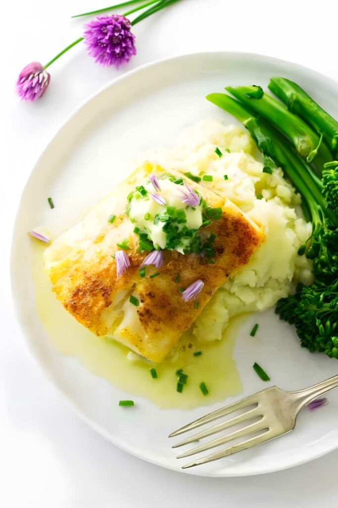 Broiled fish with herbs, mashed potatoes, vegetables, and a fork on the plate.