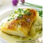 Broiled cod with chives on mashed potatoes with buttery sauce.