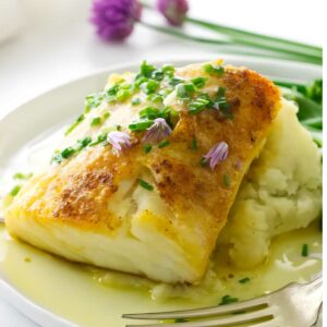 Baked fish with chives and purple flowers on mashed potatoes with buttery sauce.
