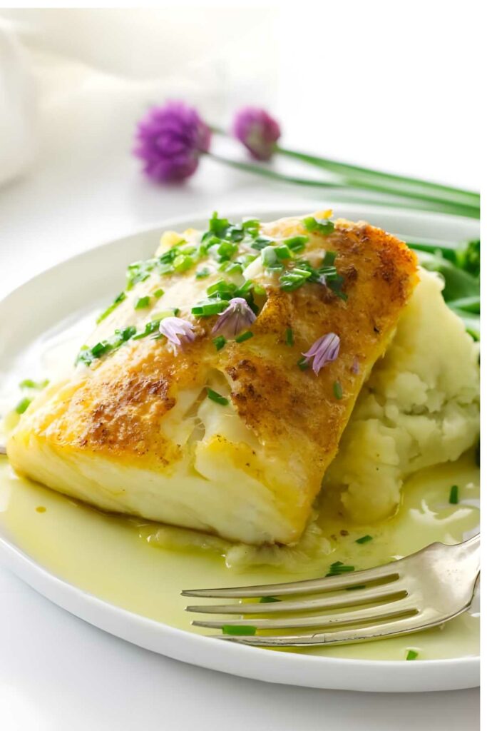 Baked fish with chives and purple flowers on mashed potatoes with buttery sauce.