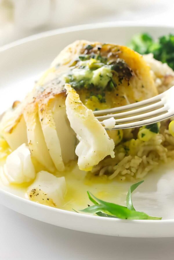 Fork cutting into baked cod with lemon tarragon sauce on rice.