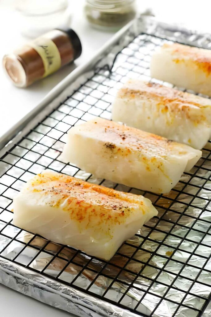 Seasoned cod fillets on a wire rack, ready to bake.