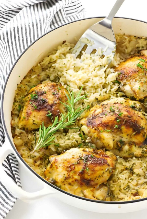 Baked chicken thighs on seasoned rice in a white pot, garnished with herbs.