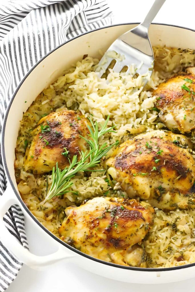 Baked chicken thighs on seasoned rice in a white pot, garnished with herbs.