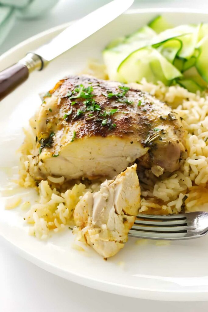 Cooked chicken and rice with herbs, fork and cucumbers on the plate.
