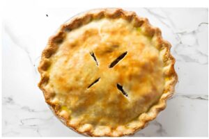 Golden-brown pie with flaky crust and slits, on a marble surface.