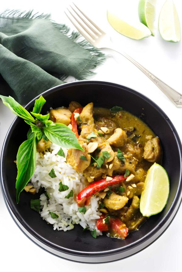 Black bowl with rice, yellow curry chicken, red peppers, herbs, and peanuts.