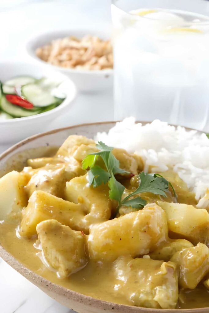 Yellow chicken and potato curry with rice, cilantro garnish, and assorted side dishes.